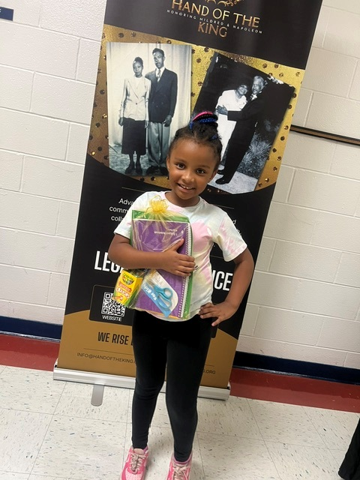 Child holding donated items in front of a Hand of the King banner