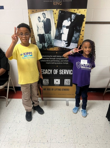 Two children posing in front of a community event banner