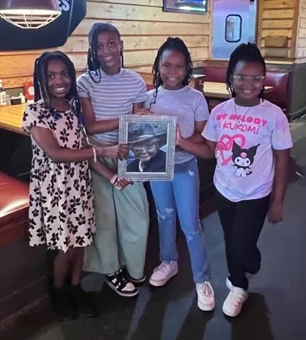 Four girls holding a framed portrait together at a community gathering