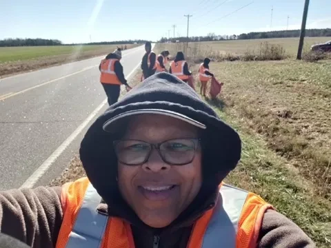 Volunteer taking a selfie with a roadside cleanup crew in the background