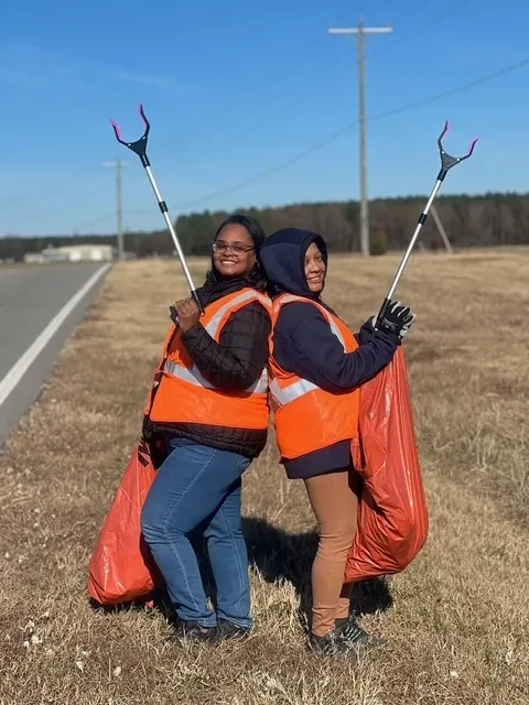 Two volunteers in reflective safety vests holding litter grabbers during a cleanup