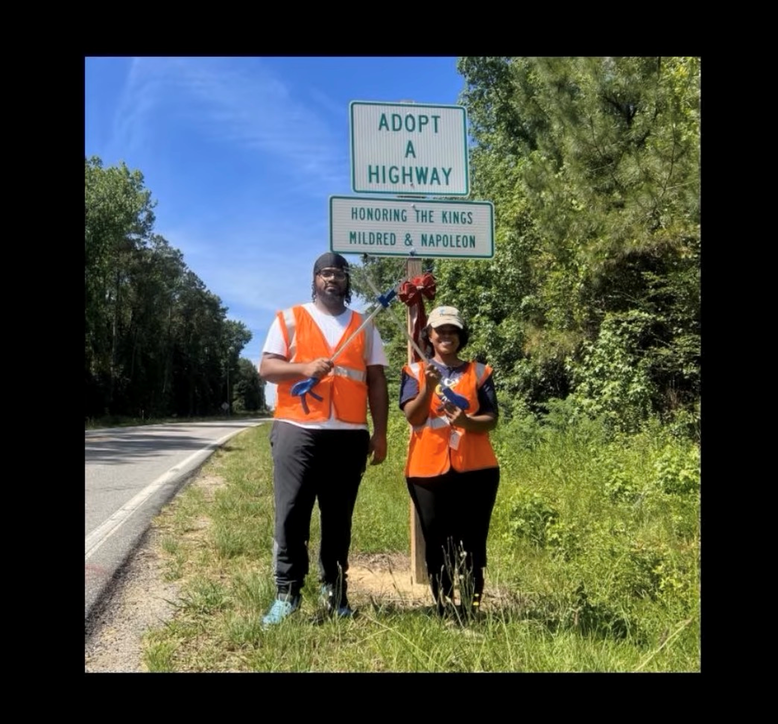 Two volunteers in safety vests beside the Adopt a Highway sign honoring Mildred and Napoleon King