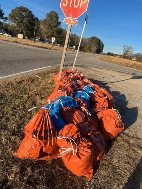 Filled cleanup bags gathered beside a roadside stop sign