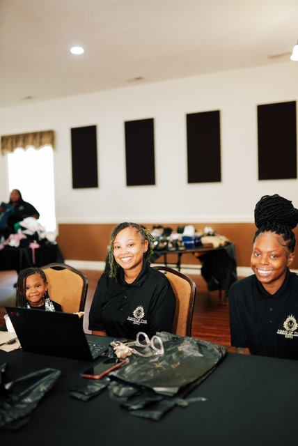 Three Hand of the King volunteers smiling at a registration table during the Clothing Giveaway