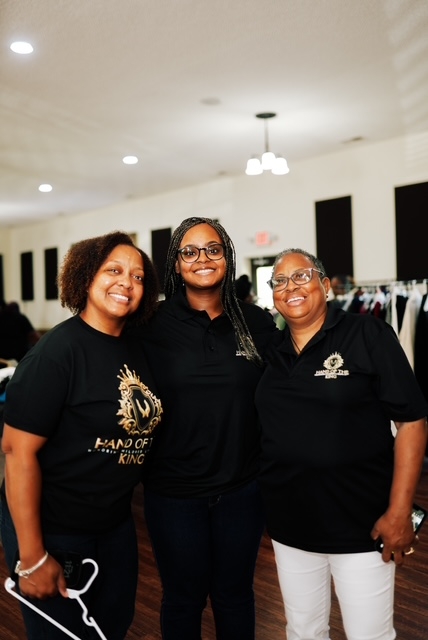 Three Hand of the King volunteers smiling together at the Clothing Giveaway