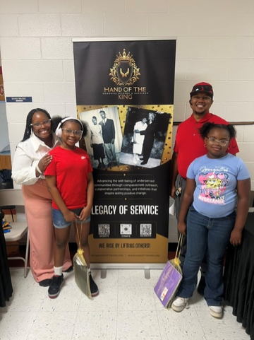 Family members posing beside a Hand of the King Legacy of Service banner