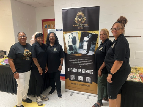 Hand of the King team members posing beside a Legacy of Service banner