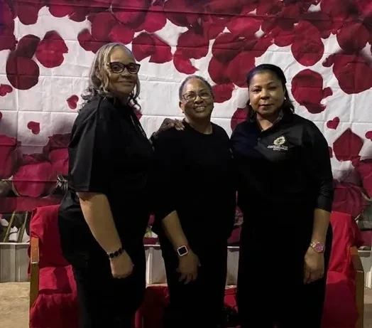 Three community members posing in front of a red and white floral backdrop