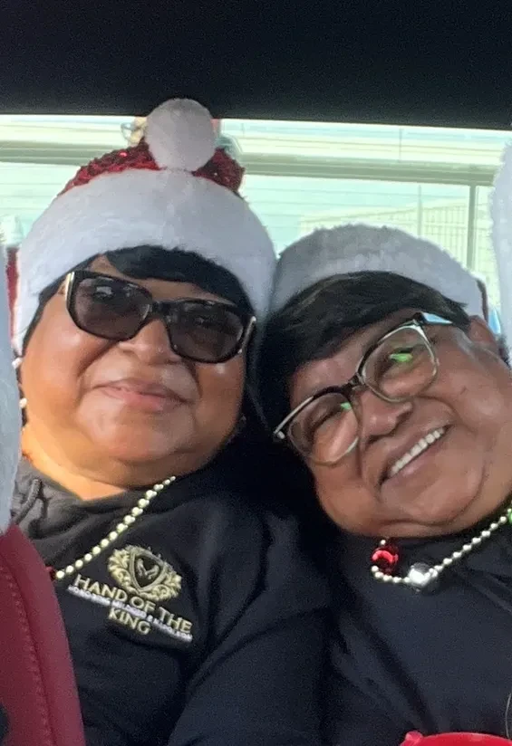 Two smiling Hand of the King volunteers wearing festive hats